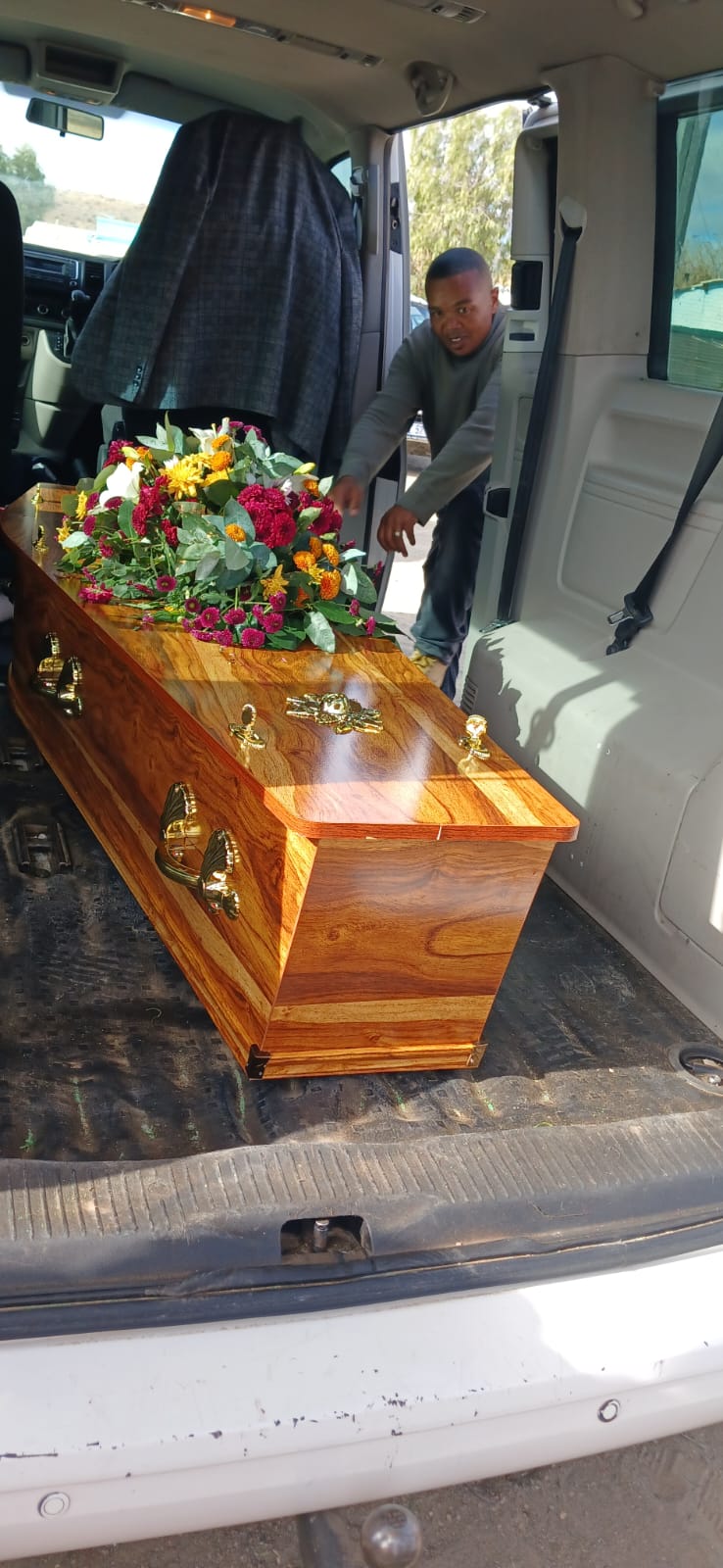Polished wooden casket with floral tribute in the G.H.G. vehicle